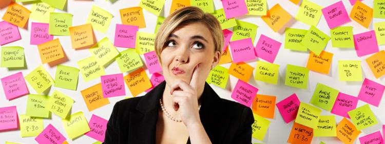 A woman stands in front of a wall of post-it note reminders, wondering.