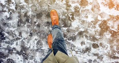 Feet of a man walking along the icy pavement. Who’s Responsible for an Icy Sidewalk Slip and Fall?
