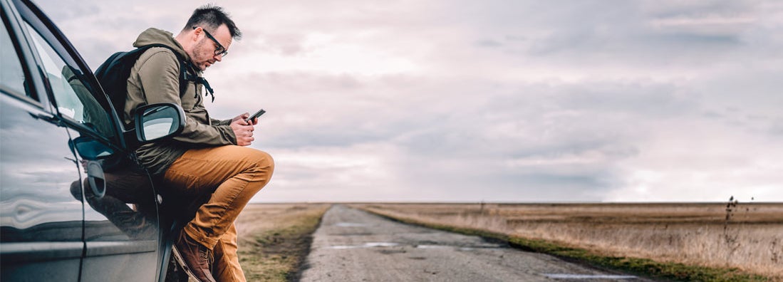 Man sitting on the car and using smart phone to research car insurance discounts