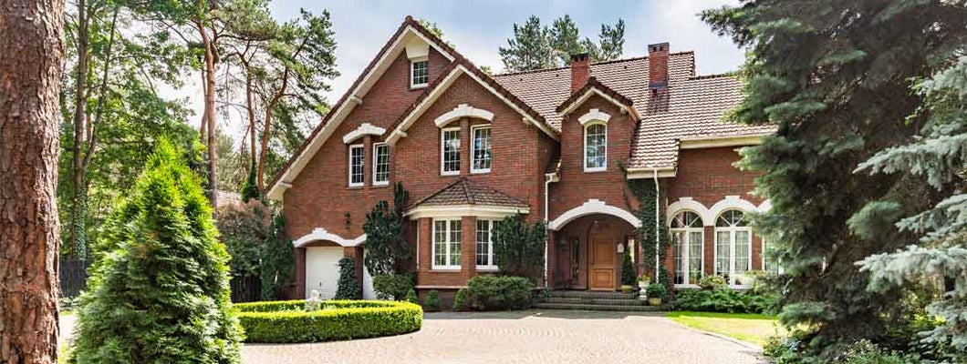 Cobbled driveway in front of a red brick English design mansion surrounded by old trees. Find Dwelling Insurance.