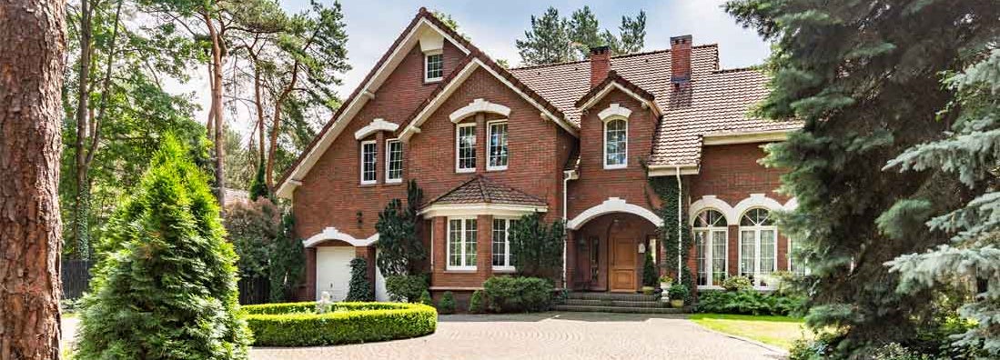 Cobbled driveway in front of a red brick English design mansion surrounded by old trees. Find Dwelling Insurance.