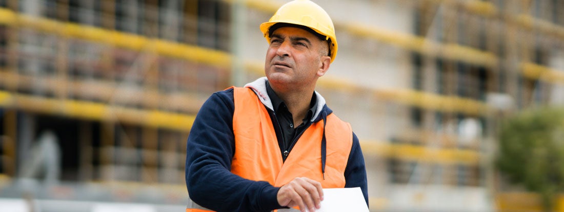 General contractor wearing protective vest and hardhat at work on construction site. Find general contractor license requirements by state.