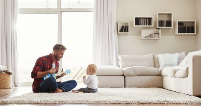 Father playing ukulele with young son in their living room. Find Universal Life Insurance. 
