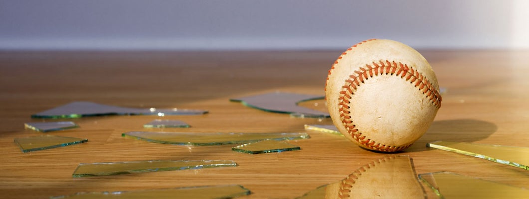Baseball with Broken Window glass on wood floor. Homeowners Insurance for Non-Auto Accidents Away from Home.