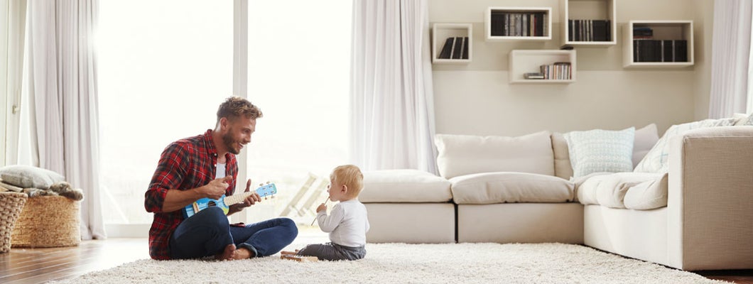 Father playing ukulele with young son in their living room. Find Universal Life Insurance.