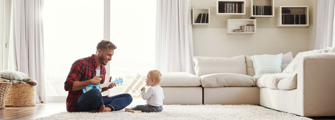 Father playing ukulele with young son in their living room. Find Universal Life Insurance.
