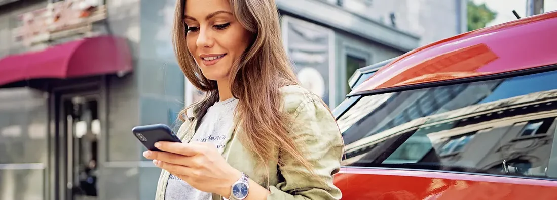 Woman using mobile phone while charging electric car. How to Find the Best Car Insurance Coverage in Fairfax, Virginia.