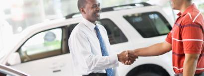 Two men shaking hands on a successful negotiation in a used car dealership.