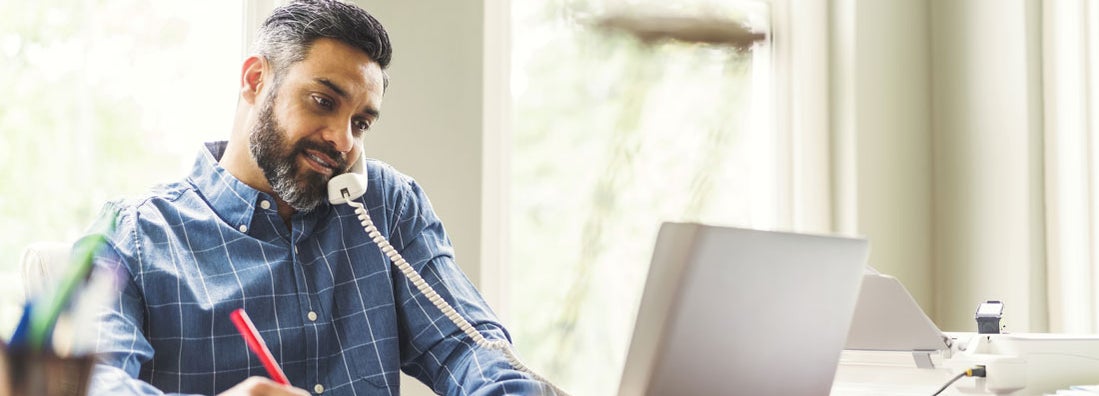 Businessman using phone and laptop at home office. Find Bluffton, South Carolina business insurance.