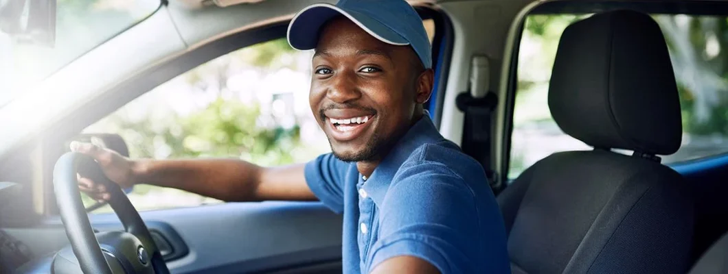 Portrait of a young postal working sitting in his car during a delivery. Find New Jersey Commercial Vehicle Insurance.