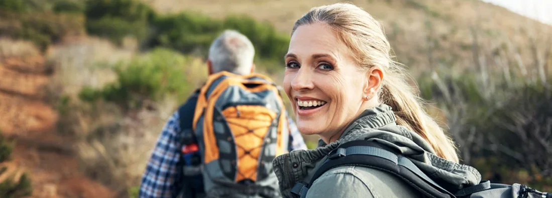 Portrait of a mature woman hiking with her husband through the mountains. Whole Life vs Term Life Insurance.