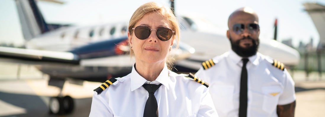 Two airplane pilots in a hangar and looking at camera. Find Pilot Insurance.