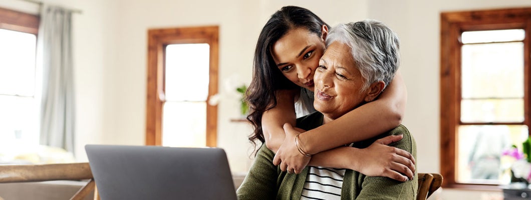 Woman hugging her mother before helping her with her finances on a laptop. Find Dallas Texas life insurance.