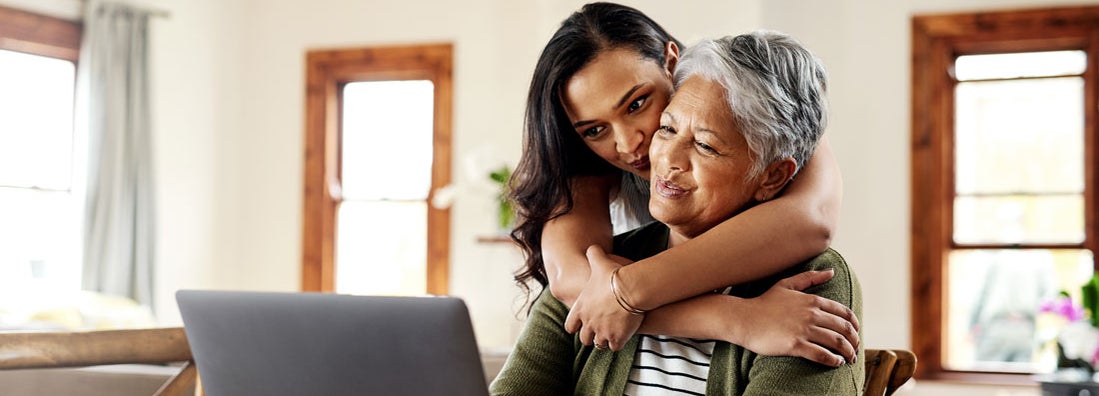 Woman hugging her mother before helping her with her finances on a laptop. Find Dallas Texas life insurance.