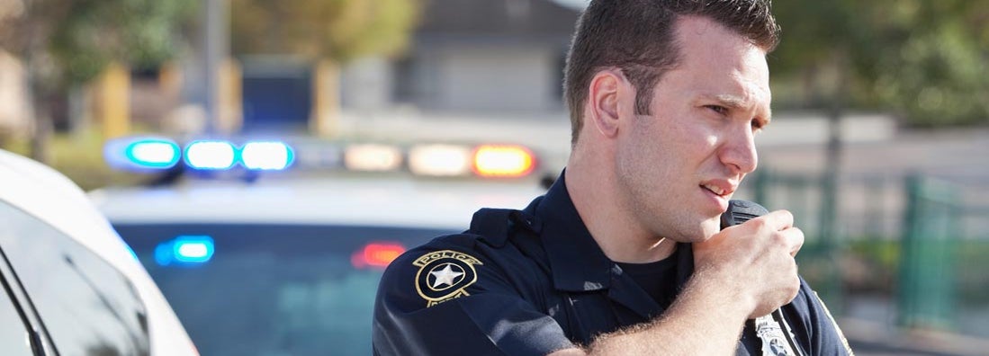 Police officer reaching for radio. Police car in background.