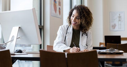 Doctor reviews her patient's records on her computer in her office. Find doctors liability insurance.