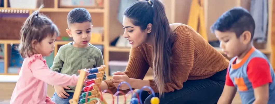 Daycare teacher sits on the floor with students as they play. Find Preschool & Daycare Insurance.