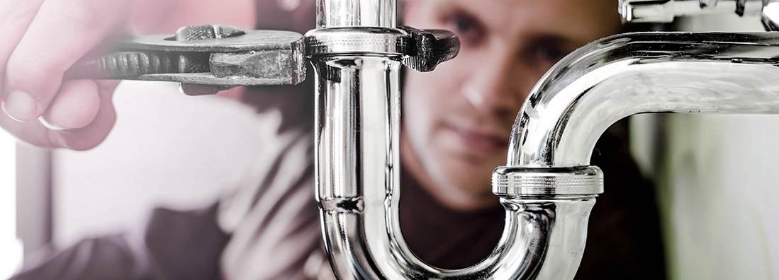 Plumber using a wrench to tighten a siphon under a sink. Find Plumbing Insurance.