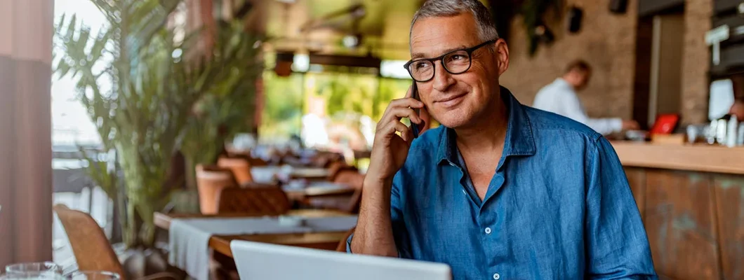 Mature man using smartphone and laptop computer in cafe. How to Buy Business Insurance.