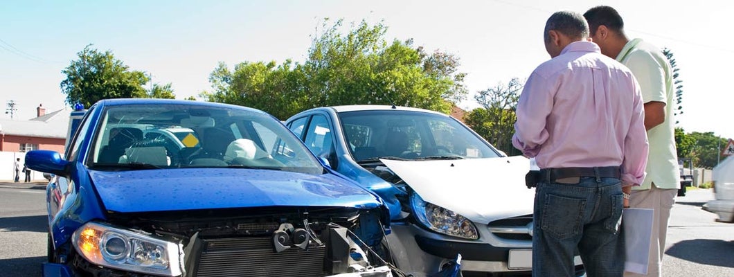 Two men conferring next to car accident. What happens if an at-fault driver doesn't have insurance.