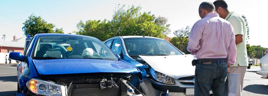 Two men conferring next to car accident. What happens if an at-fault driver doesn't have insurance.