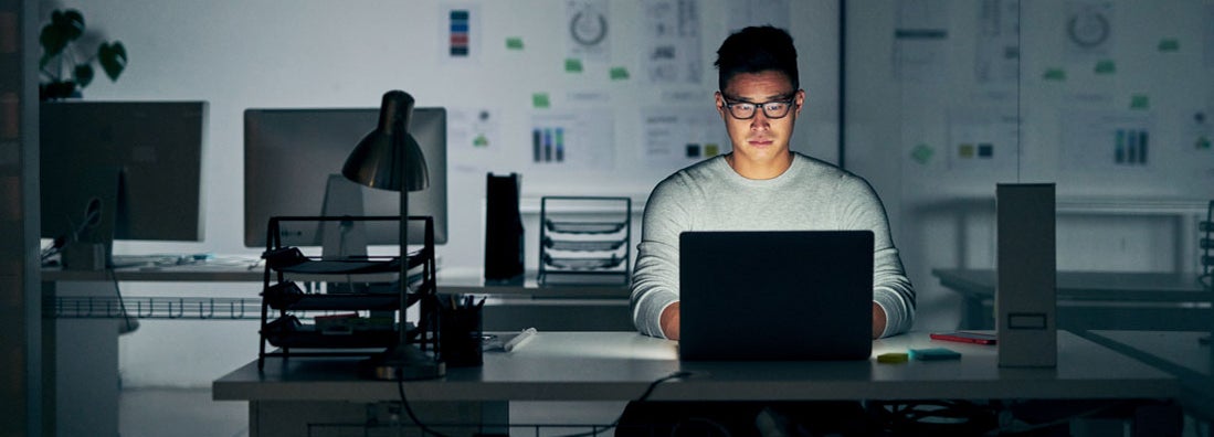 Businessman using a laptop during a late night in a modern office. Understanding Why Your Business Needs Cyber Liability Insurance.
