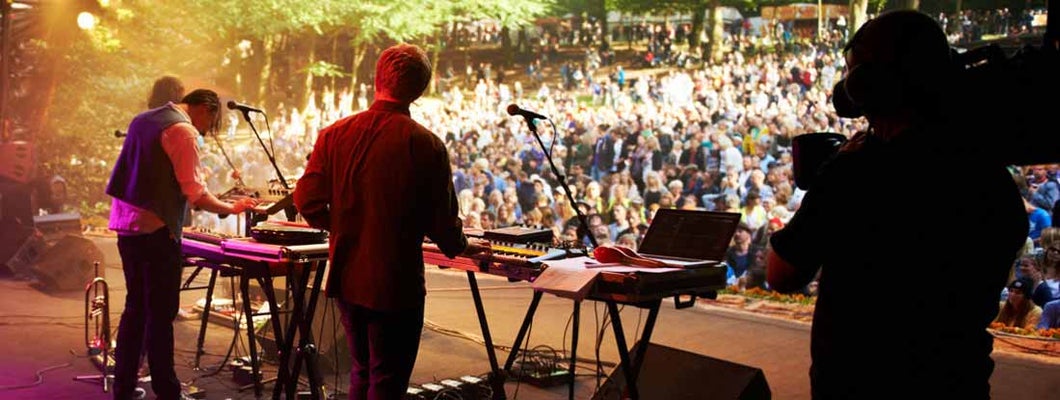 Rearview shot of a band on stage at an outdoor music festival. Find Musicians Insurance.