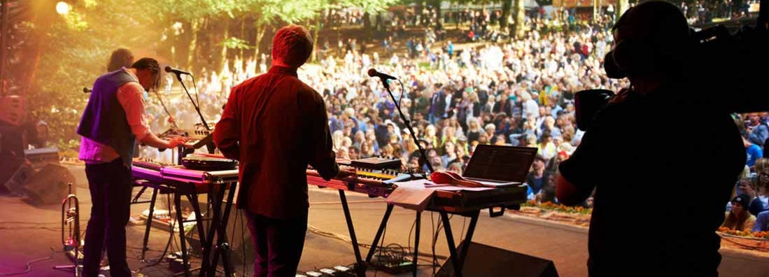 Rearview shot of a band on stage at an outdoor music festival. Find Musicians Insurance.