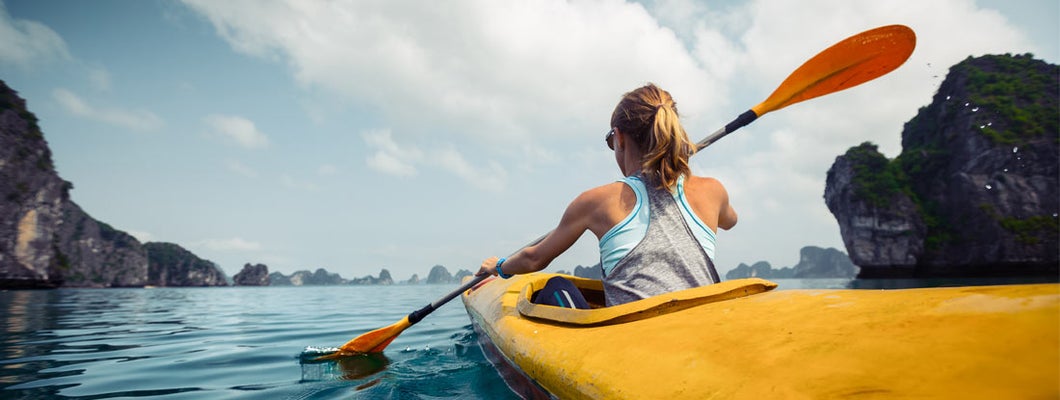 Woman exercising and exploring calm tropical bay by kayak.