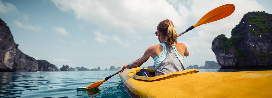 Woman exercising and exploring calm tropical bay by kayak.
