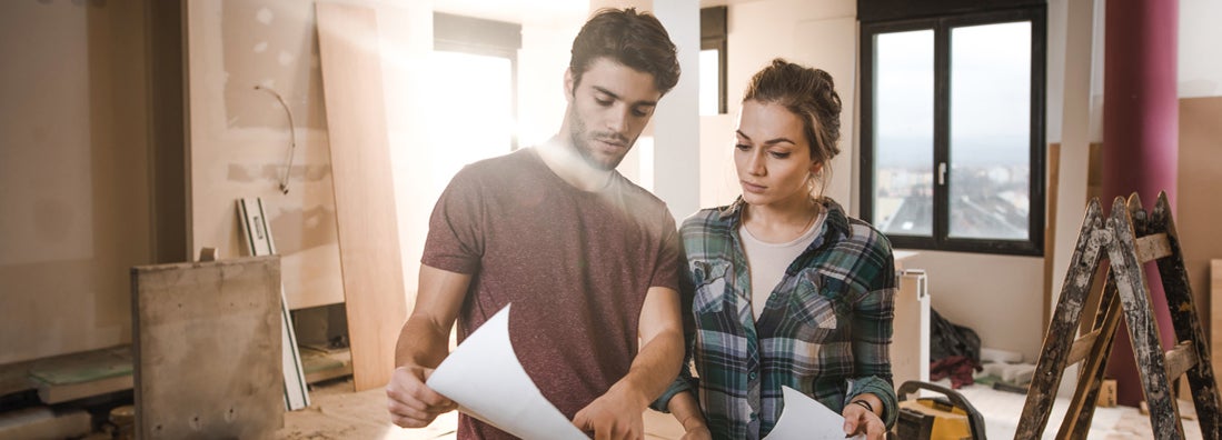 Young couple examining blueprints while being on construction site in their home