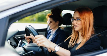 Woman learning how to drive car with her instructor. Find your learners permit insurance.