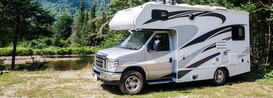 RV parked in forest besides a river . Find RV Insurance Cost. 