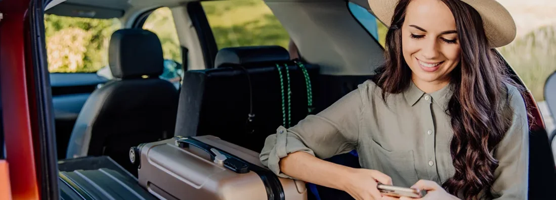 Woman sitting in car trunk full of luggage and using phone. Cody, Wyoming Car Insurance. 