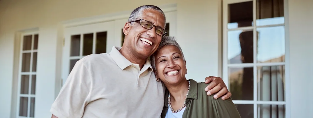Senior couple smile outside of their home. The difference between landlord and homeowners insurance.