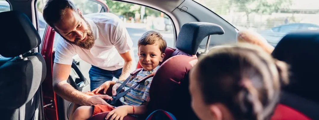 Father putting his kids in carseats to be safe during road trip. The 10 Safest Cars.