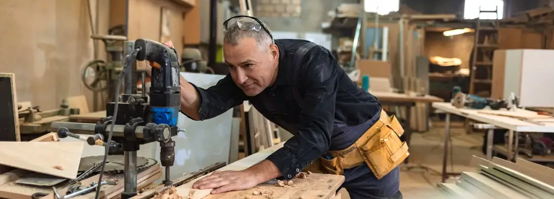 Carpenter using drill press in workshop. Find Cumberland Hill, Rhode Island business insurance.