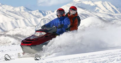 Couple Snowmobiling with Mountains in the background. The Best Snowmobile Destinations in the US.