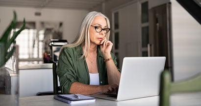 Focused mature woman with white hair at home using laptop