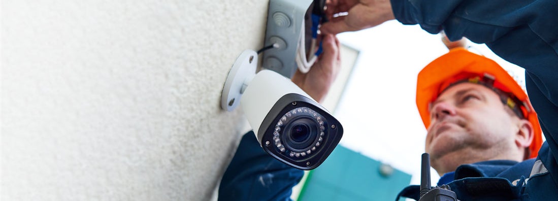 Security company employee installing video surveillance camera on wall