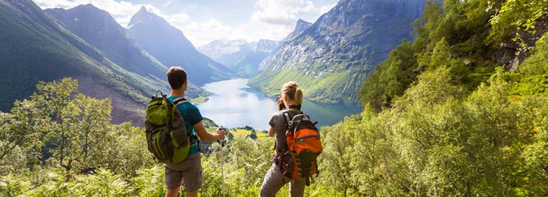 Two hikers at viewpoint in mountains with lake, sunny summer