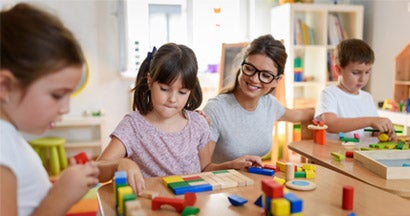 Preschool teacher with children playing with colorful wooden blocks at school. Find Teacher Home Insurance Discounts. 