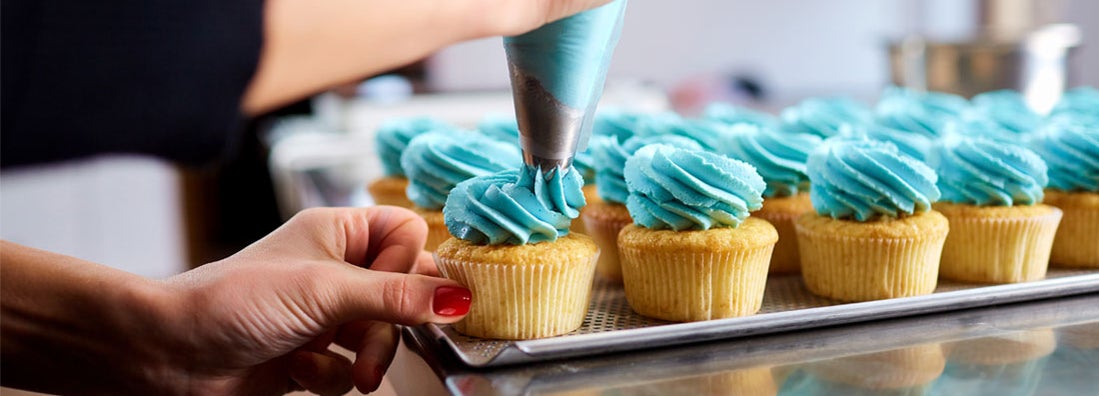 Woman in bakery icing cupcakes. Find business liability insurance.