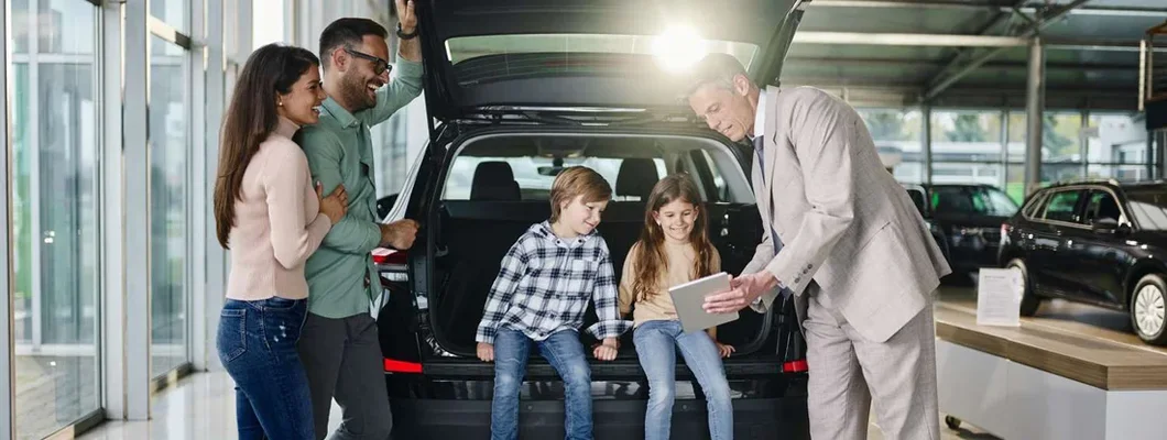 Family and salesperson using digital tablet in a car showroom. Same day car insurance.