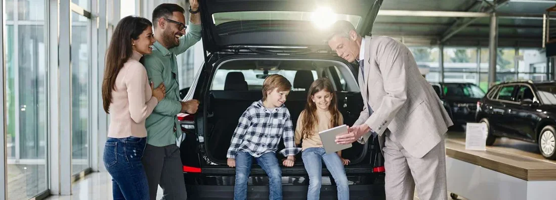 Family and salesperson using digital tablet in a car showroom. Same day car insurance.