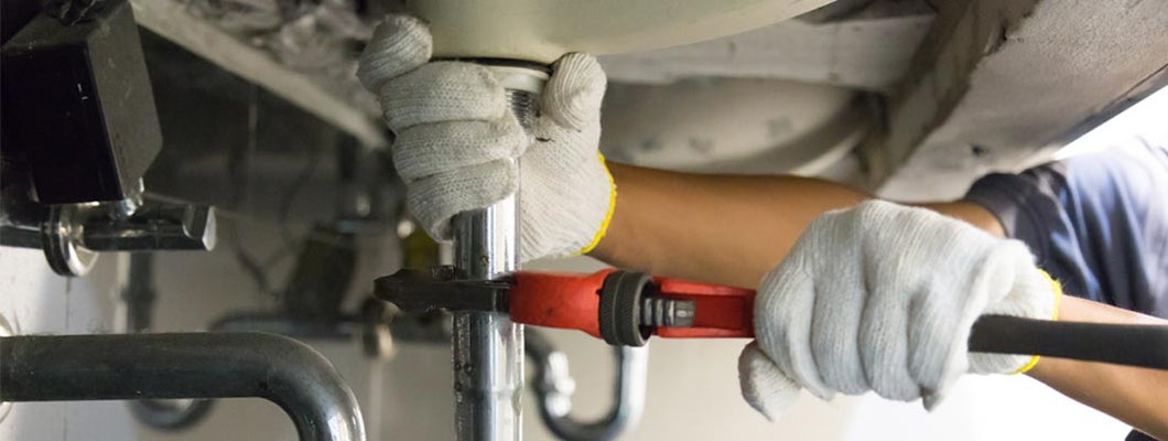 Plumber using a wrench to tighten a siphon under a sink. Find Home Repair Insurance.