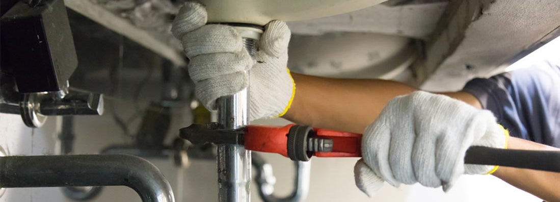 Plumber using a wrench to tighten a siphon under a sink. Find Home Repair Insurance.
