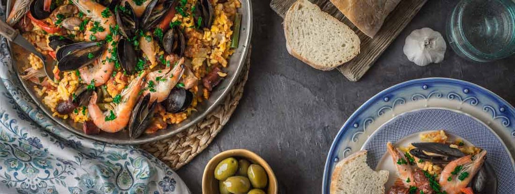 Paella with olives and bread on stone table