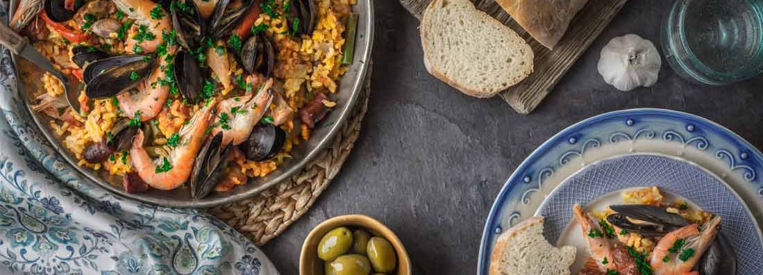 Paella with olives and bread on stone table