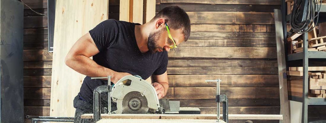 A man builder saws a board with a circular saw in the workshop. Find Carpenter Liability Insurance.